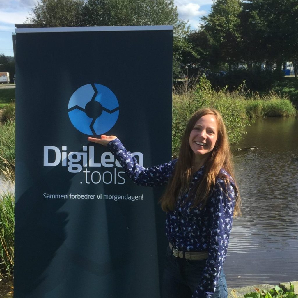 Caucasian woman presenting DigiLEAN.tools in front of roll-up poster outside next to water pond