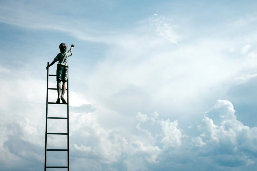 A boy on the top of a ladder going up towards the sky.